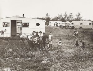 Black and white photograph of a group of people stood outside caravans in a field.