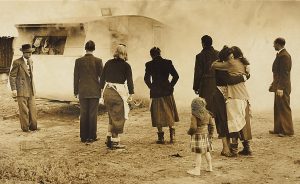 Photograph of people in a group stood outside watching a caravan burn.