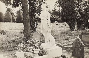 Black and white photograph of a statue and pots of flowers on a grave.