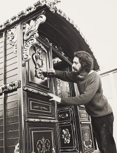 Black and white photograph of a person restoring the exterior of an old-style caravan.