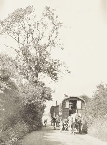 Photograph of an old-style horse drawn caravan coming down a country road.