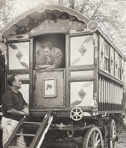 Black and white photograph of person leaning out of their old-style caravan talking to another person stood outside.