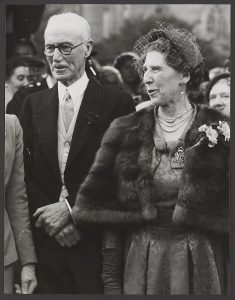 Black and white photo of a man in a suit with glasses and a woman in a dress outside